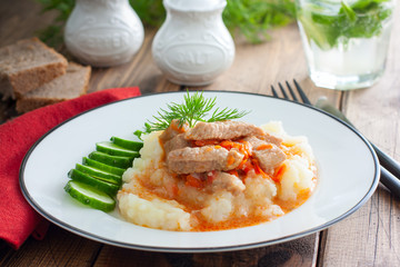 Pork slices with tomato sauce and mashed potatoes on a wooden table, horizontal