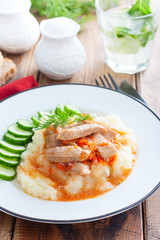 Pork with gravy and mashed potatoes and fresh cucumber on a wooden table, selective focus