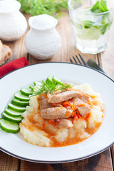 Pork with gravy and mashed potatoes and fresh cucumber on a wooden table, selective focus
