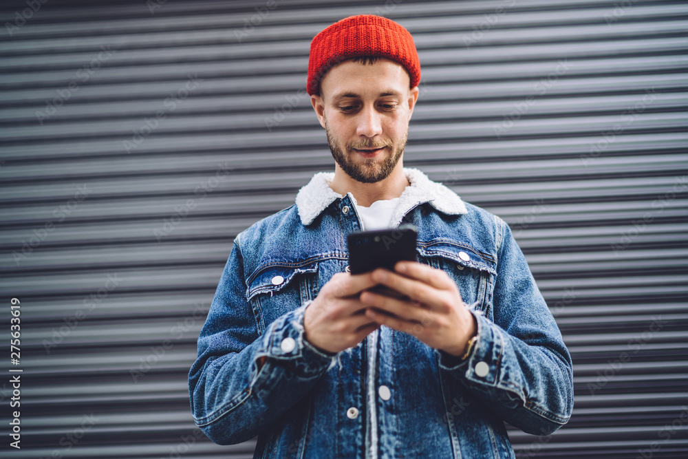 Poster handsome male blogger checking public comments in social networks while standing at urban setting wi