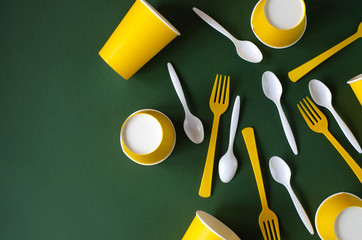 Flat lay plastic and paper utensils on a green background.