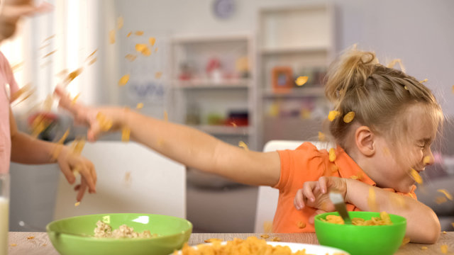 Happy little boy and girl throwing cornflakes at each other, having fun at home