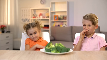 Kids looking with disgust at broccoli, unappetizing meal, tasteless healthy food