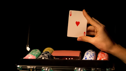 Hand showing ace card, betting in poker, gambling addiction, suitcase with chips