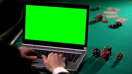 Male gambler betting poker online on laptop, holding lucky dice, green screen