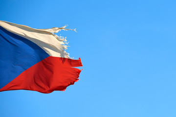 Tattered Czech Republic flag against blue sky blowing in the wind with copy space