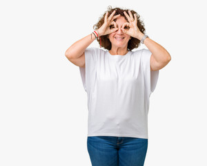 Beautiful middle ager senior woman wearing white t-shirt over isolated background doing ok gesture like binoculars sticking tongue out, eyes looking through fingers. Crazy expression.