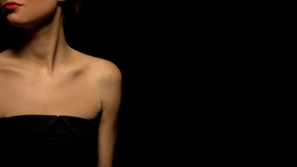 Woman in seductive black dress standing against black background, prostitution