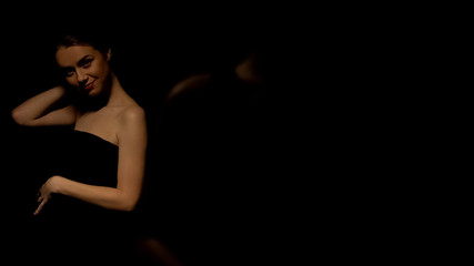 Sexy woman in dress posing for camera, isolated on black background, seduction