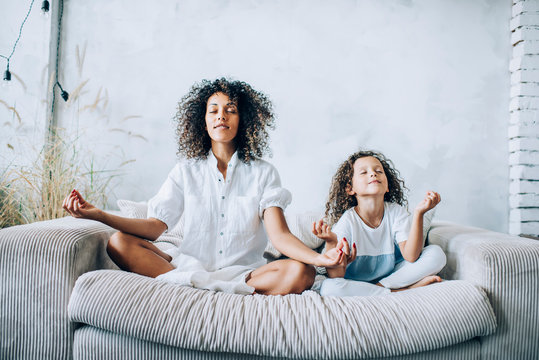 Cute girl and mother meditating on couch