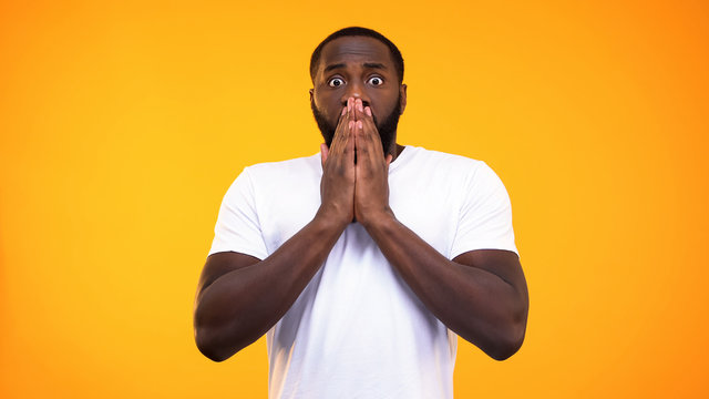 Young surprised black man closing his mouth with hands on yellow background