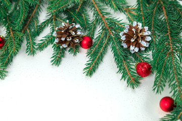 New Year's background on white. Branches a fir-tree with small red Christmas balls and cones. In the center of composition the place for an inscription. On all background small snowflakes.