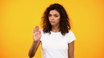 Serious biracial woman showing no gesture on camera against yellow background