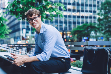 Positive male entrepreneur with digital tablet looking away and smiling while sitting at urban...