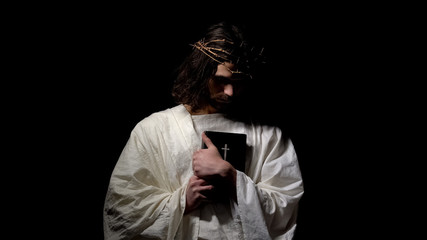 Male alike Jesus Christ standing in darkness holding holy bible, confession