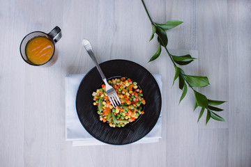 Frozen fried vegetables on black plate. Vegan breakfast with juice. Vegetables food mix on white wooden background with plant.