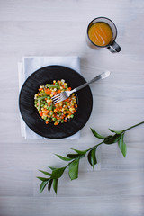 Frozen fried vegetables on black plate. Vegan breakfast with juice. Vegetables food mix on white wooden background with plant.