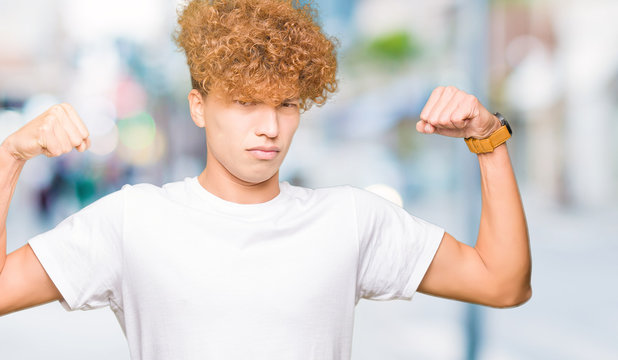 Young handsome man with afro hair wearing casual white t-shirt showing arms muscles smiling proud. Fitness concept.