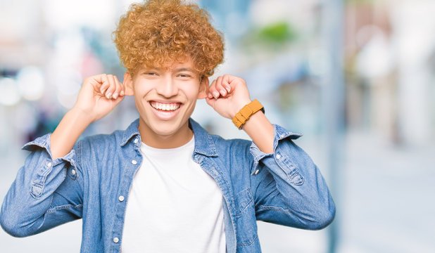 Young handsome man with afro hair wearing denim jacket Smiling pulling ears with fingers, funny gesture. Audition problem