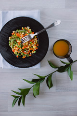 Frozen fried vegetables on black plate. Vegan breakfast with juice. Vegetables food mix on white wooden background with plant.