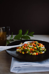 Frozen fried vegetables on black plate. Vegan breakfast. Vegetables food mix on white wooden background with plant.