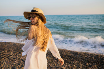 Young happy attractive girl in hat having fun at the beach. Blue waves on the background.