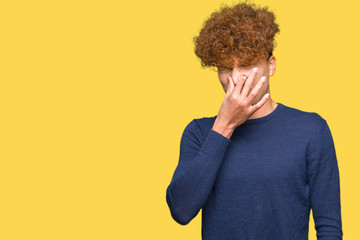 Young handsome man with afro hair smelling something stinky and disgusting, intolerable smell,...