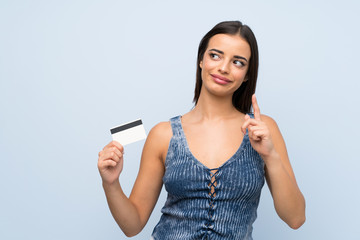 Young woman over isolated blue wall holding a credit card