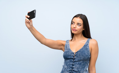 Young woman over isolated blue wall making selfie with cellphone