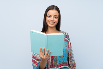 Obraz premium Young woman over isolated blue wall holding and reading a book