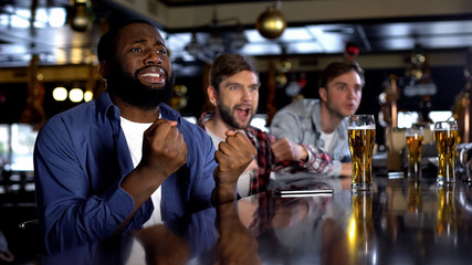 Overemotional afro-american man cheering for favorite team with friends in bar