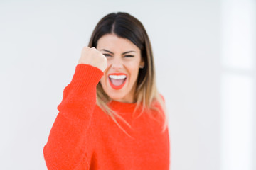 Young woman wearing casual red sweater over isolated background angry and mad raising fist frustrated and furious while shouting with anger. Rage and aggressive concept.