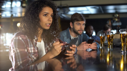 Anxious multiethnic sports fans monitoring bets in phones in pub, expecting win