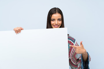 Young woman over isolated blue wall holding an empty white placard for insert a concept