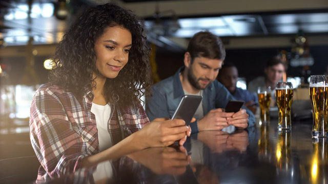 Multiracial people scrolling phones in pub instead of communication, addiction