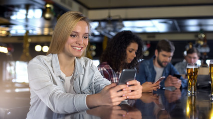 Blond lady chatting in phone in bar, reading messages in dating app, free wi-fi