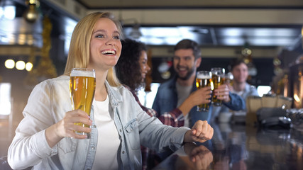 Happy friends raising glasses of beer for victory in game, live program in bar