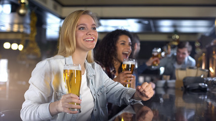 Blond lady cheering for national team, raising glass of beer for victory in game