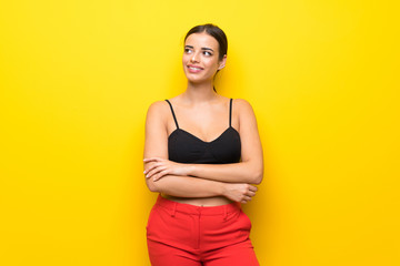Obraz premium Young woman over isolated yellow background looking up while smiling