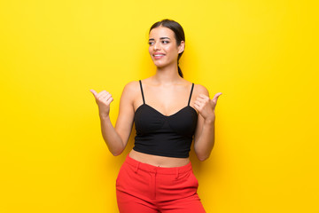 Young woman over isolated yellow background with thumbs up gesture and smiling