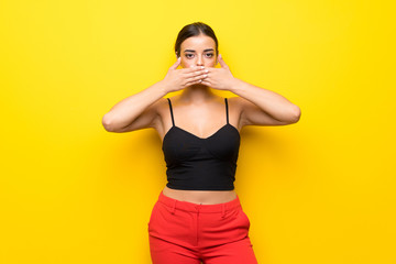 Young woman over isolated yellow background covering mouth with hands