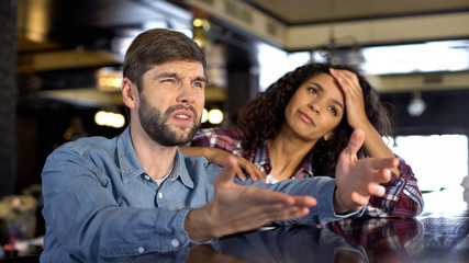 Multi-ethnic couple watching sport competition, looking upset, disappointment