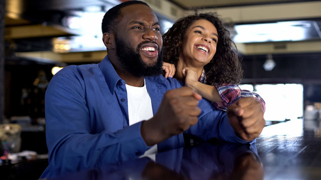 Happy mixed-race couple supporting national team watching game, entertainment