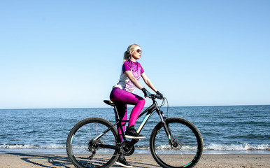 Fototapeta na wymiar sporty girl on a sports bike rides a bicycle by the sea, healthy lifestyle of a young girl