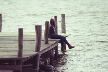 Young adult woman sitting on a wooden jetty on the river