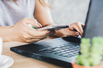 woman hand using smart phone and typing on keyboard of computer laptop at desk 