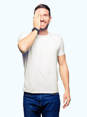 Fototapeta premium Handsome man wearing casual white t-shirt covering one eye with hand with confident smile on face and surprise emotion.