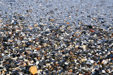 Wet seashells and small stones in sea water surf of Black sea coastline. Natural beach pebble texture. Travel background. Sea vacation backdrop.  