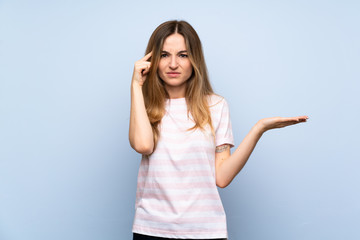 Young woman over isolated blue background making the gesture of madness putting finger on the head