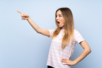 Young woman over isolated blue background pointing away